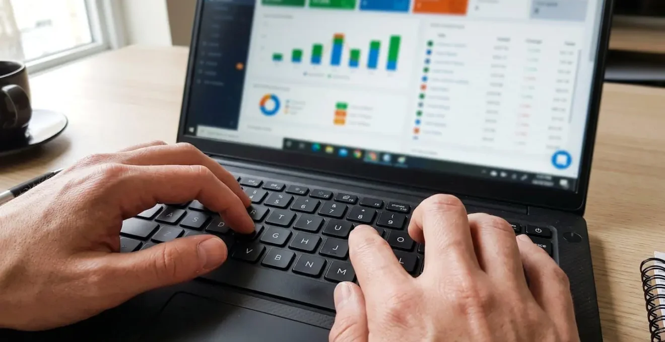 Primo piano estremo di mani che digitano su una tastiera di laptop moderno, con schermo che mostra grafici colorati completamente sfocati, su superficie di scrivania contemporanea pulita